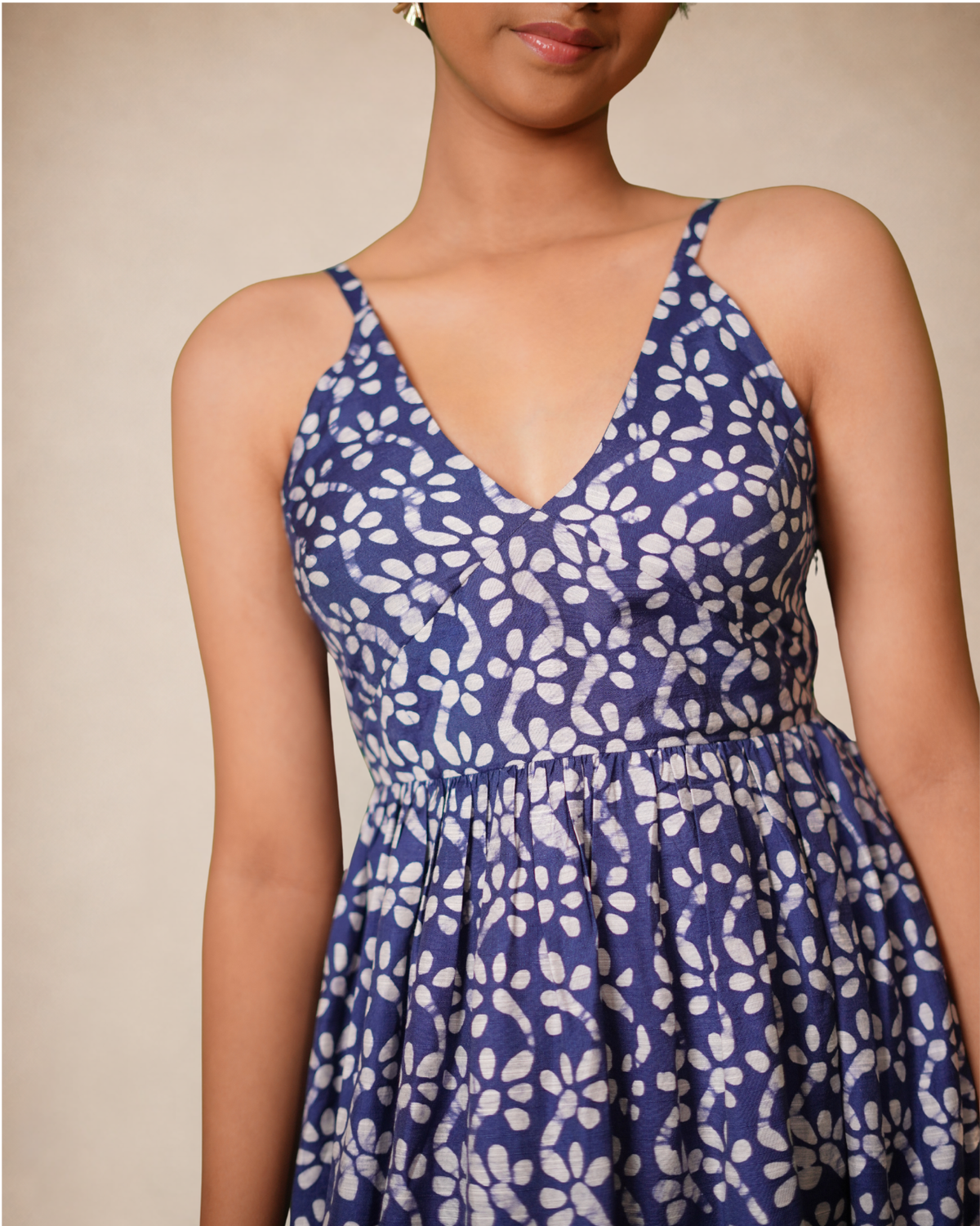A woman wearing a sleeveless V-neck dress with thin straps and a gathered waist, featuring a blue and white floral block print pattern