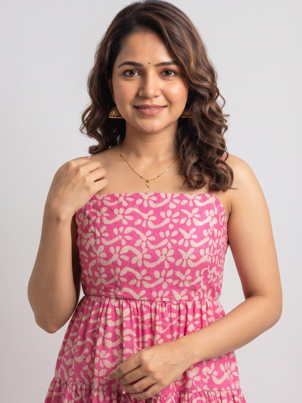 A woman wearing a pink strapless dress with a beige floral block print pattern, photographed against a light gray studio background.