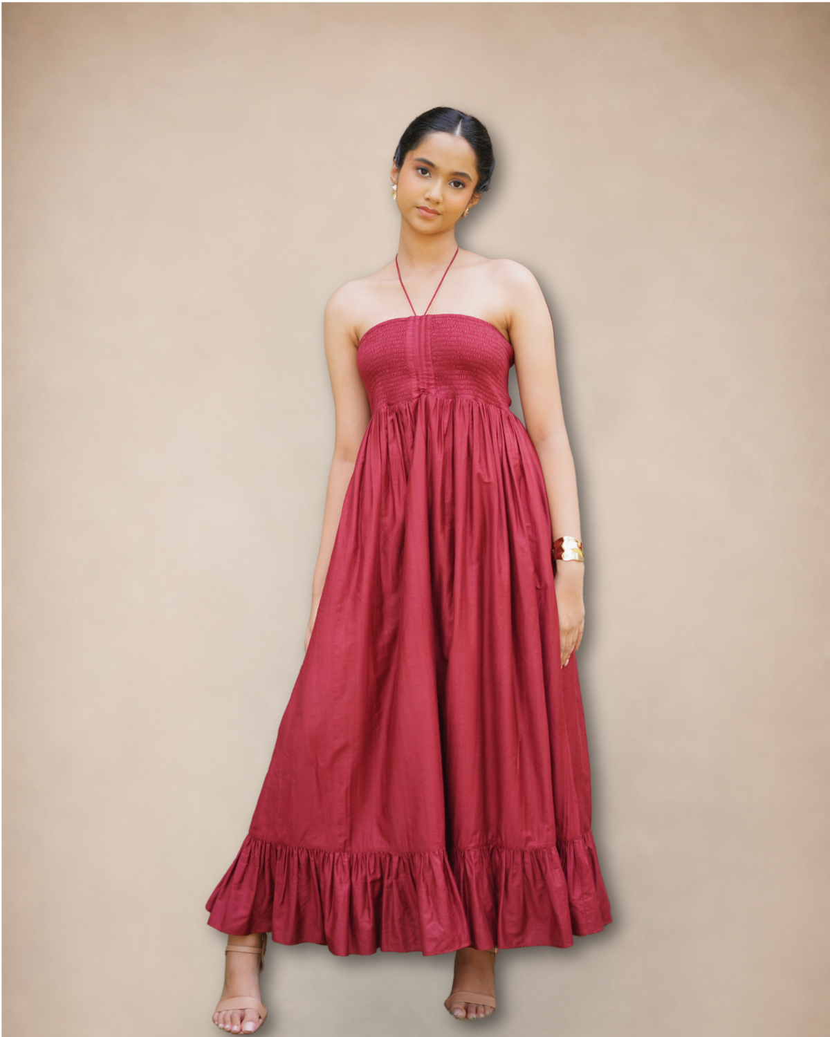 A woman modeling a strapless, floor-length magenta maxi dress with a gathered bodice and ruffled hem