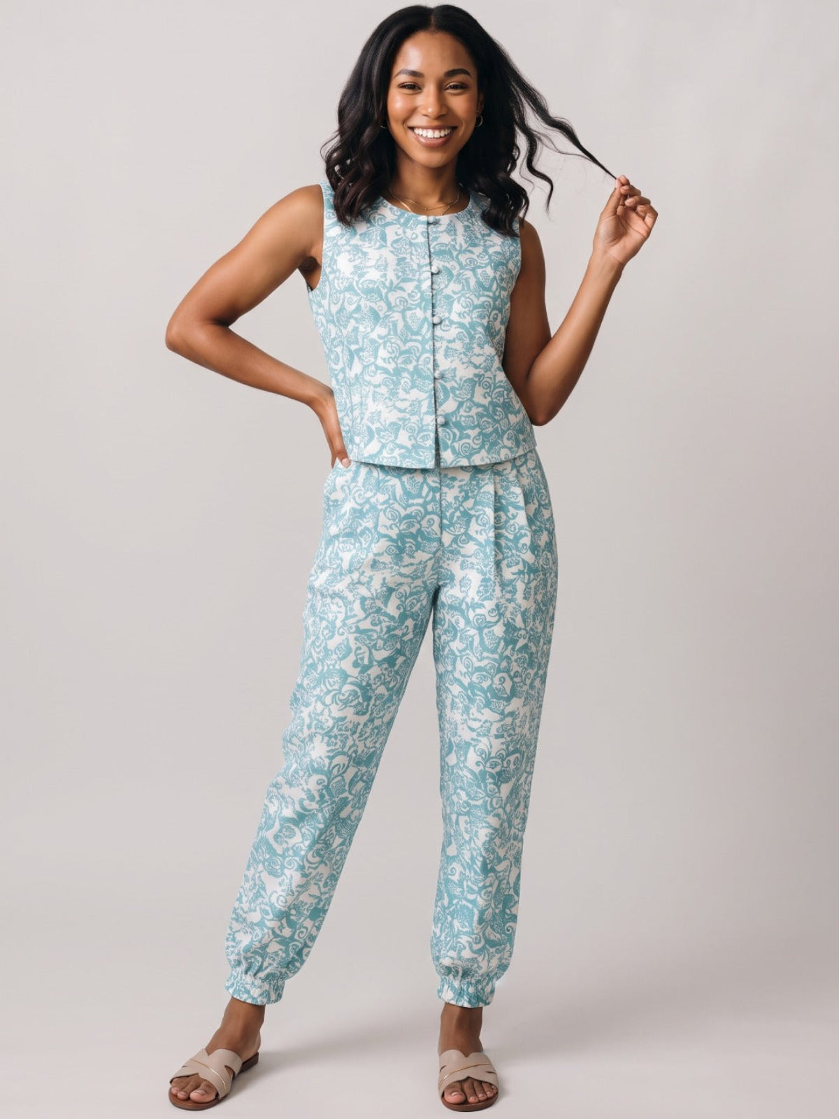 A woman modeling a matching sleeveless top and jogger pants set in a light blue and white floral print, standing against a neutral light gray studio background.