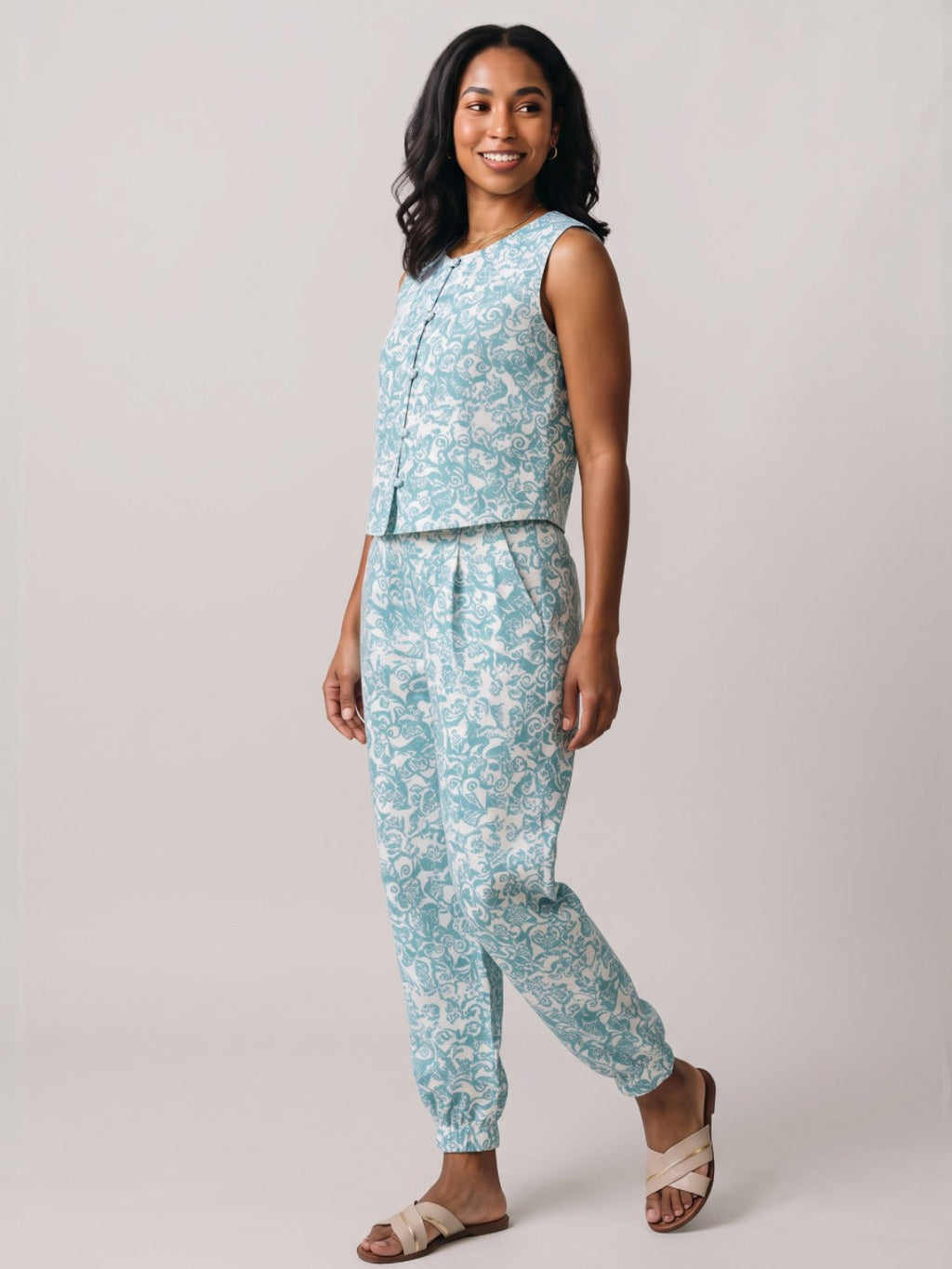 A woman modeling a sleeveless light blue and white patterned jumpsuit against a plain light gray studio background.